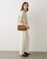 Person standing with a shoulder bag wearing a sweater and trousers.