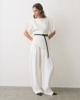 Model wearing loose pants and a top with a belt standing in a neutral setting.