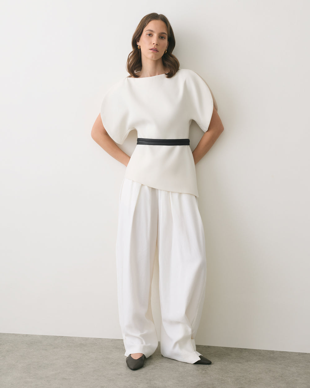 Person wearing a structured top with wide-leg pants, standing against a plain wall.