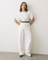 Person wearing a structured top with wide-leg pants, standing against a plain wall.