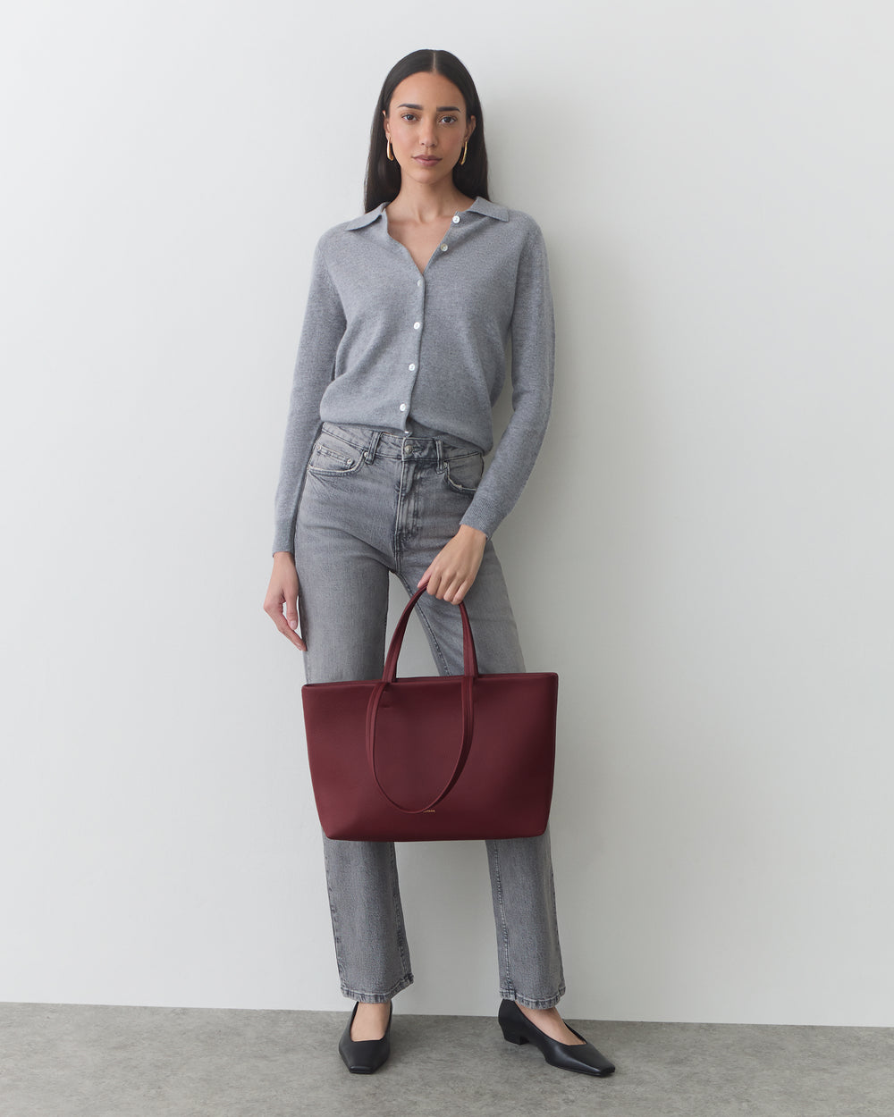 Person standing with a large tote bag, wearing a button-up shirt and jeans.