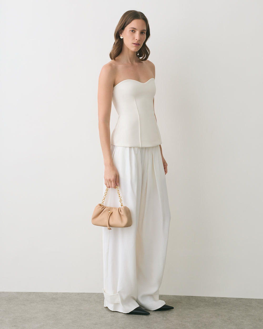 Person wearing strapless top and wide pants, holding small handbag.