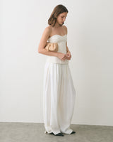 Person in strapless top and wide pants holds a clutch bag.
