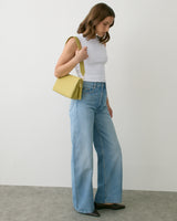 Person in sleeveless top with jeans carries shoulder bag.