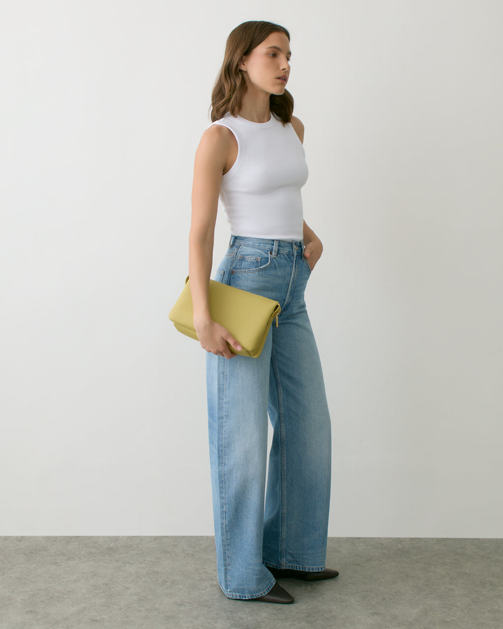 Person in sleeveless top and wide jeans holding a clutch.