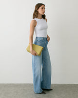Person in sleeveless top and wide jeans holding a clutch.