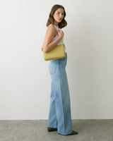 Person in jeans holding shoulder bag, standing on gray floor next to white wall.