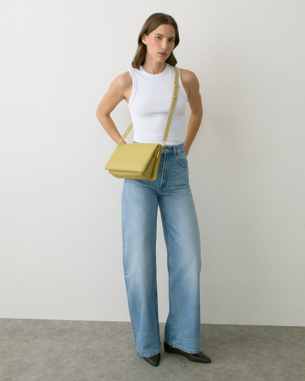 Person wearing a sleeveless top, wide-leg jeans, and a crossbody bag, standing indoors.