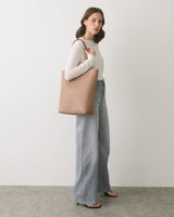 Person in white top and wide jeans carrying a tote bag standing on a grey floor.