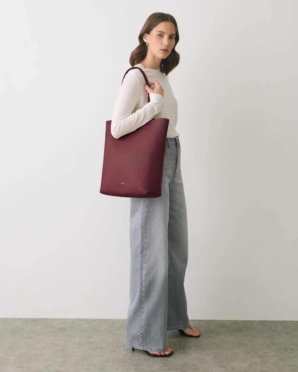 Person holding a large tote bag, wearing a long sleeve top and wide-leg jeans.