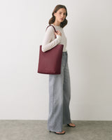 Person holding a large tote bag, wearing a long sleeve top and wide-leg jeans.