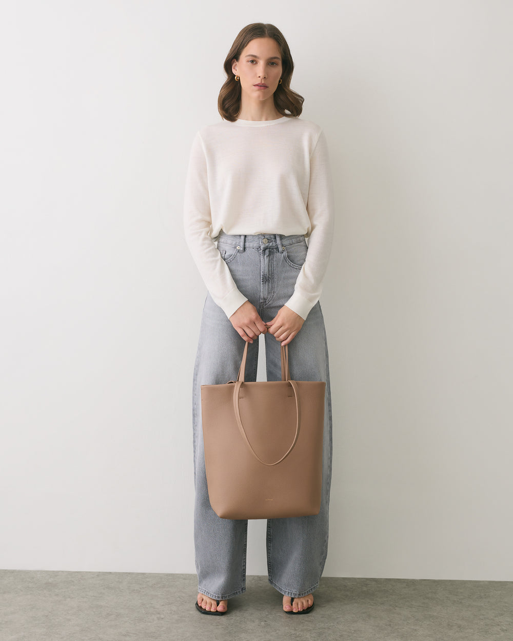 Person in casual outfit holding a tote bag standing indoors.