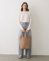 Person in casual outfit holding a tote bag standing indoors.