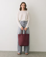 Person holding a large tote bag in both hands standing against plain background.