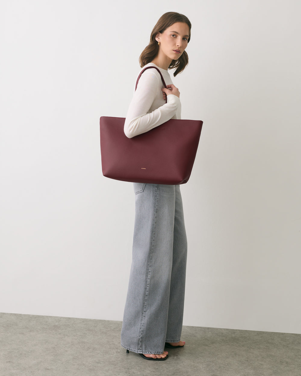 Person carrying a large tote bag over shoulder, wearing long-sleeve top and wide-leg pants.