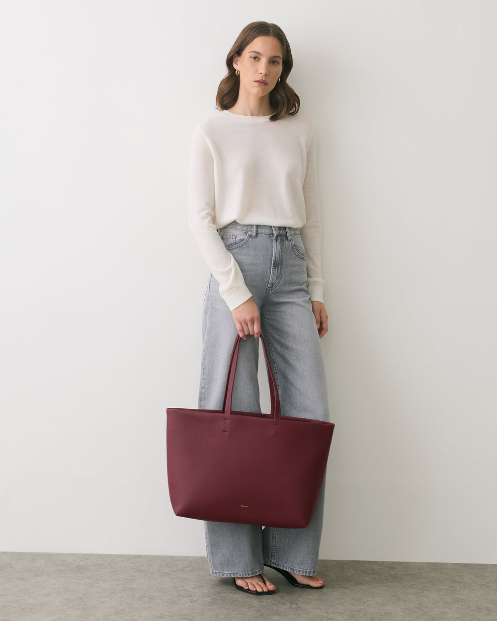 Person standing with a large handbag wearing a long-sleeve shirt and jeans.