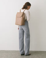 Person wearing jeans and carrying a backpack, facing a white wall.