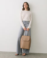 Person in sweater and jeans holds a handbag.
