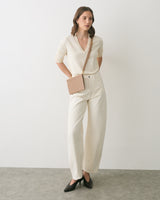 Person standing with a crossbody bag wearing a long-sleeve top and wide-leg pants.