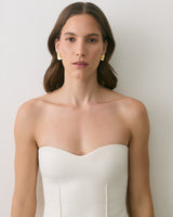 Person wearing a strapless top with gold earrings standing against a plain background.