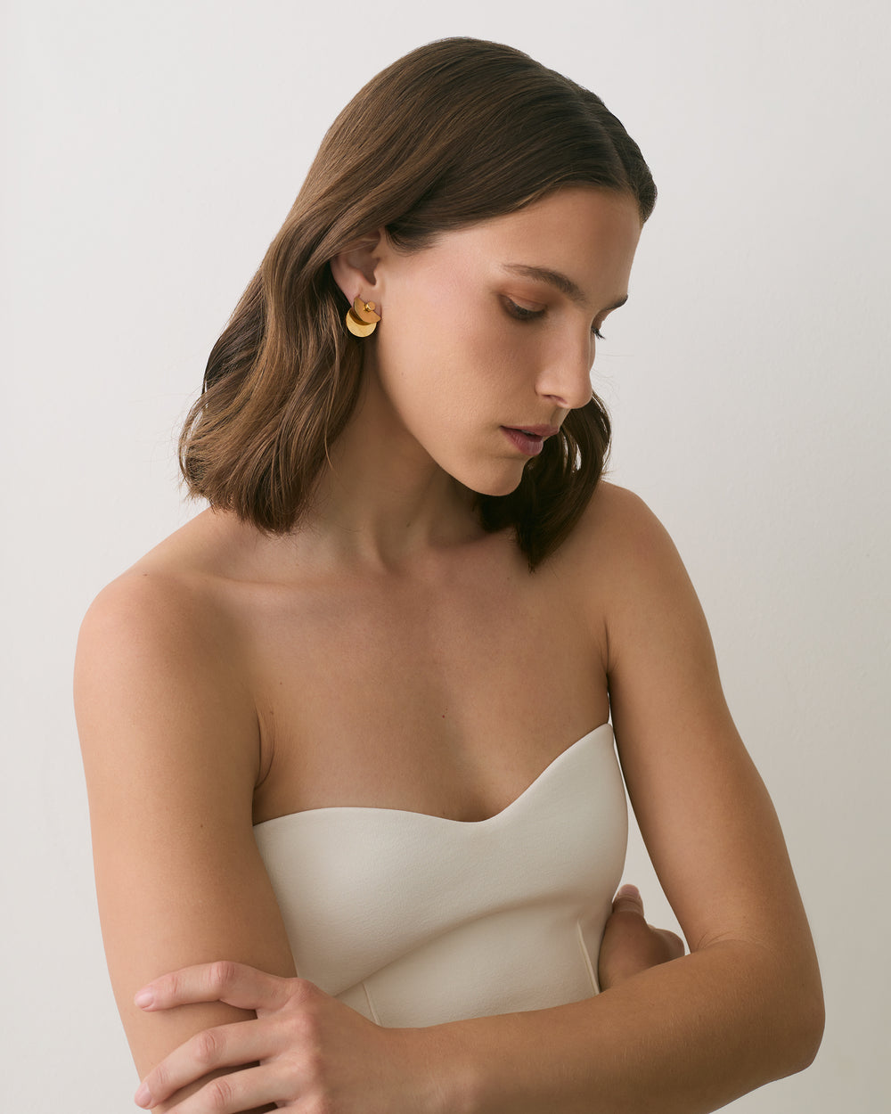 Person in strapless top with folded arms and gold earrings.