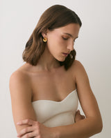 Person in strapless top with folded arms and gold earrings.