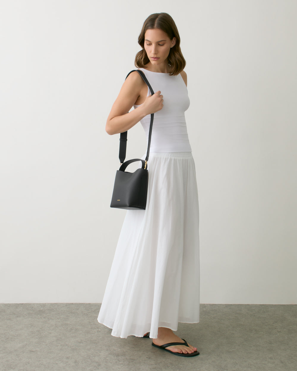 Person in sleeveless top and long skirt holding a small shoulder bag.