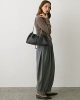 Person standing with shoulder bag wearing long pants and a sweater.