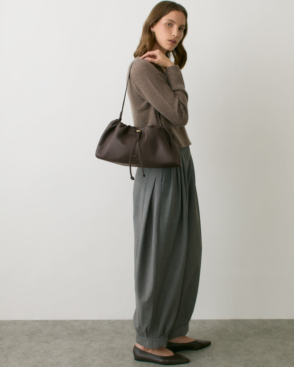 Person standing with long pants and carrying a shoulder bag.