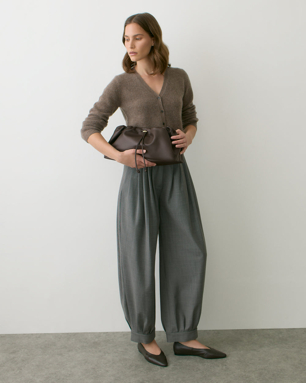 Person wearing a sweater and loose pants, holding a small bag.
