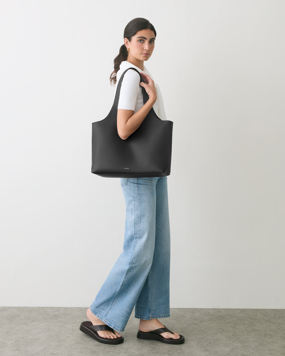 Person carrying a large tote bag standing in profile against a plain background.