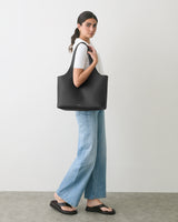 Person carrying a large tote bag standing in profile against a plain background.