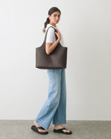 Person standing with tote bag over shoulder, wearing jeans and a t-shirt, looking at camera.