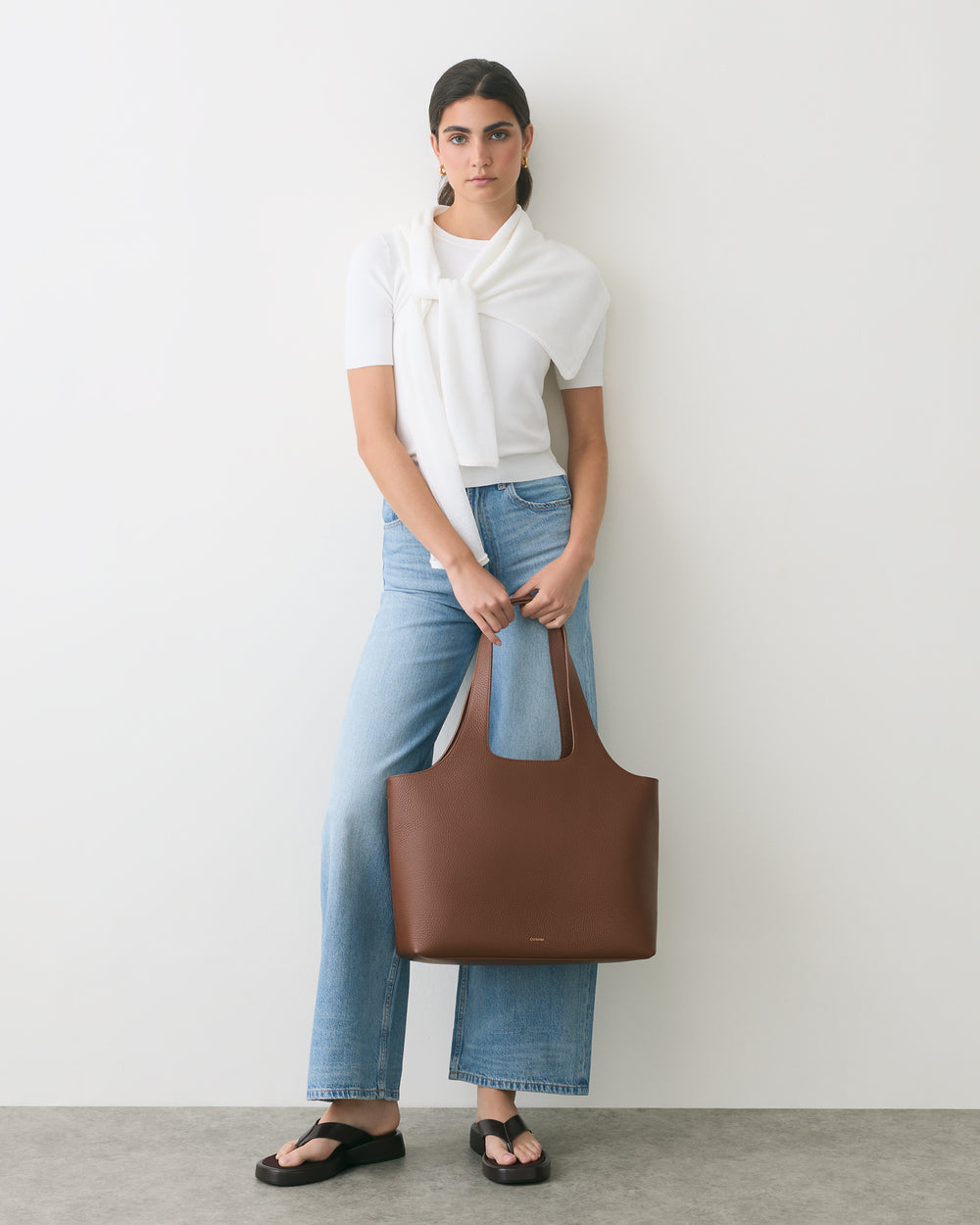 Person standing with a large handbag, wearing jeans and sandals.
