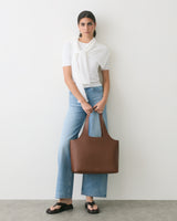 Person standing with a large handbag, wearing jeans and sandals.