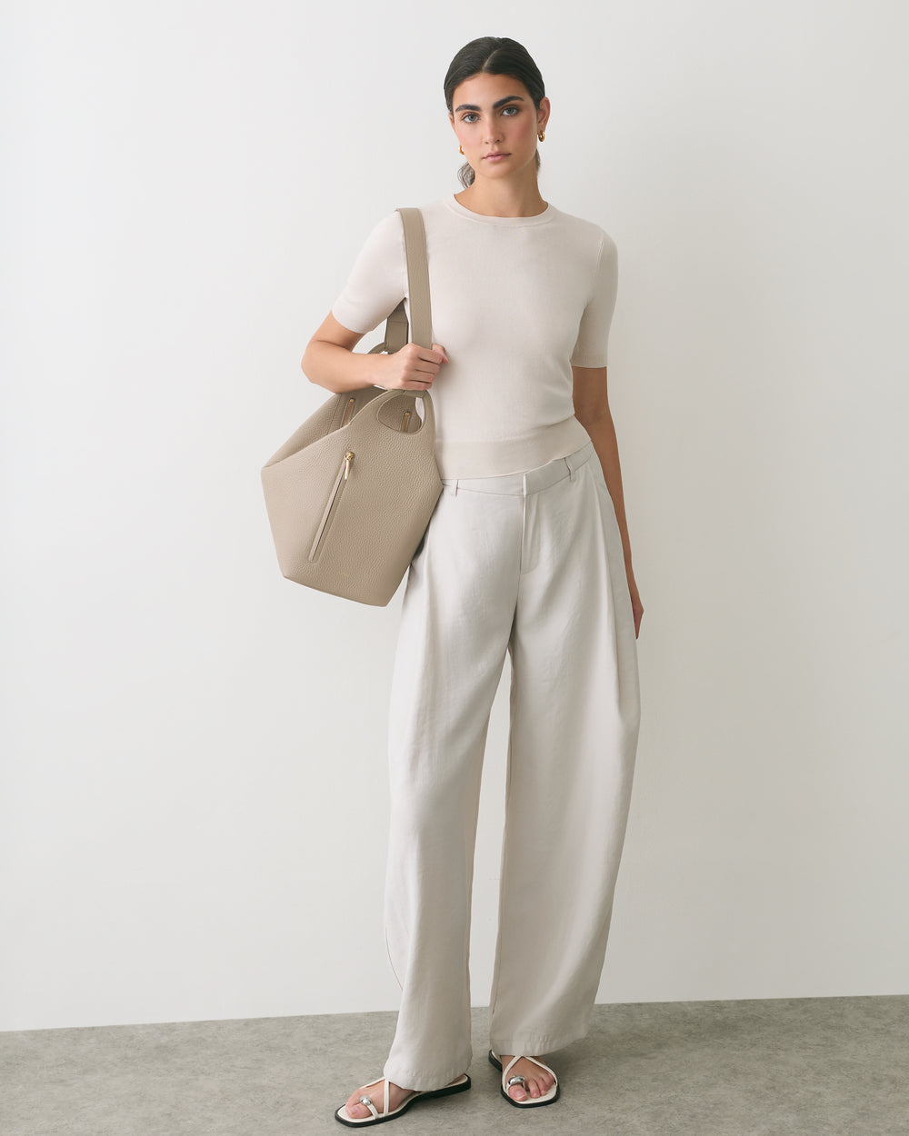 Person standing with a travel bag wearing short-sleeve shirt and wide-leg pants.