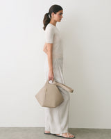 Person in profile holding a large handbag, dressed in a simple outfit with sandals.