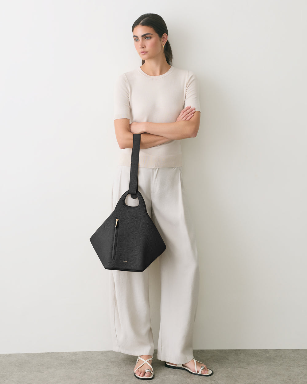 Person leans against wall holding a geometric handbag and wearing a casual outfit.