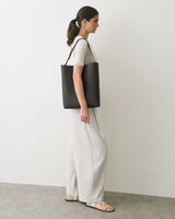 Person standing with a shoulder bag wearing a short-sleeve top and long pants.