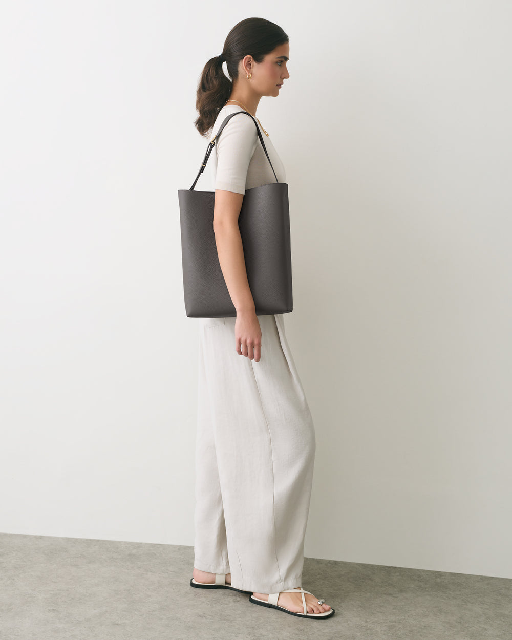 Person standing with shoulder bag, wearing a top, pants, and sandals.