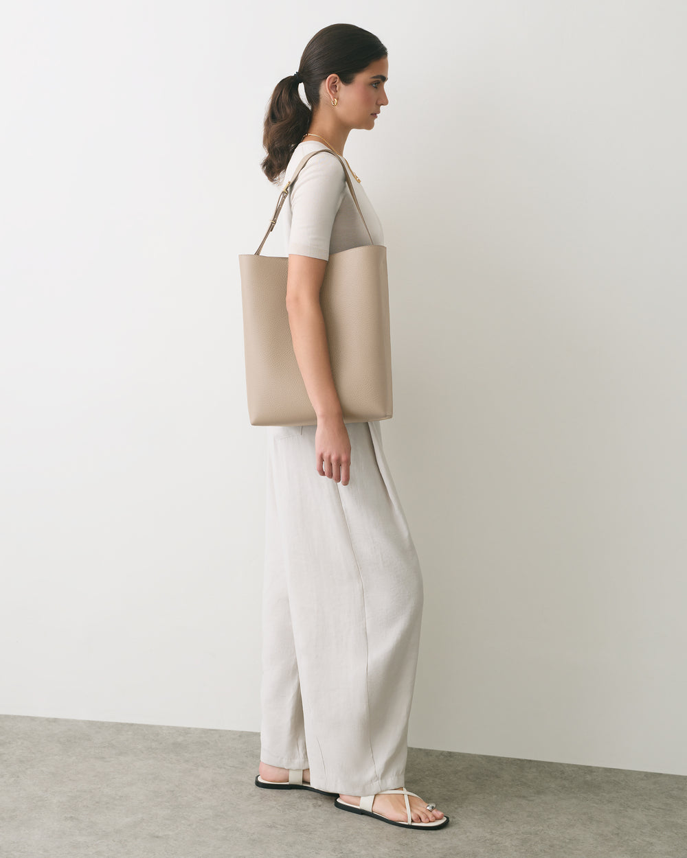 Person standing with a shoulder bag wearing a top and wide-leg pants.