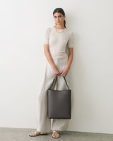 Person standing with a tote bag wearing a short-sleeve top and wide-leg pants.