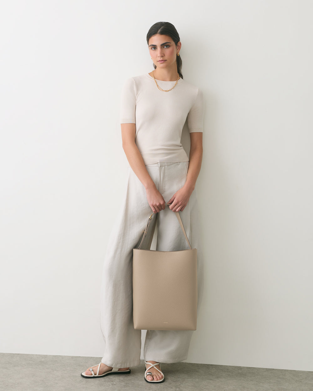Person standing with a tote bag wearing a casual outfit and sandals.
