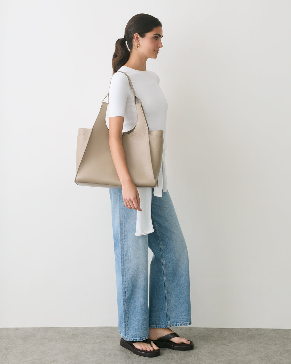 Person standing with large shoulder bag, wearing jeans and sandals.