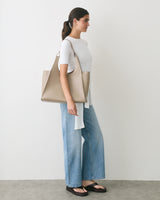 Person standing with large shoulder bag, wearing jeans and sandals.