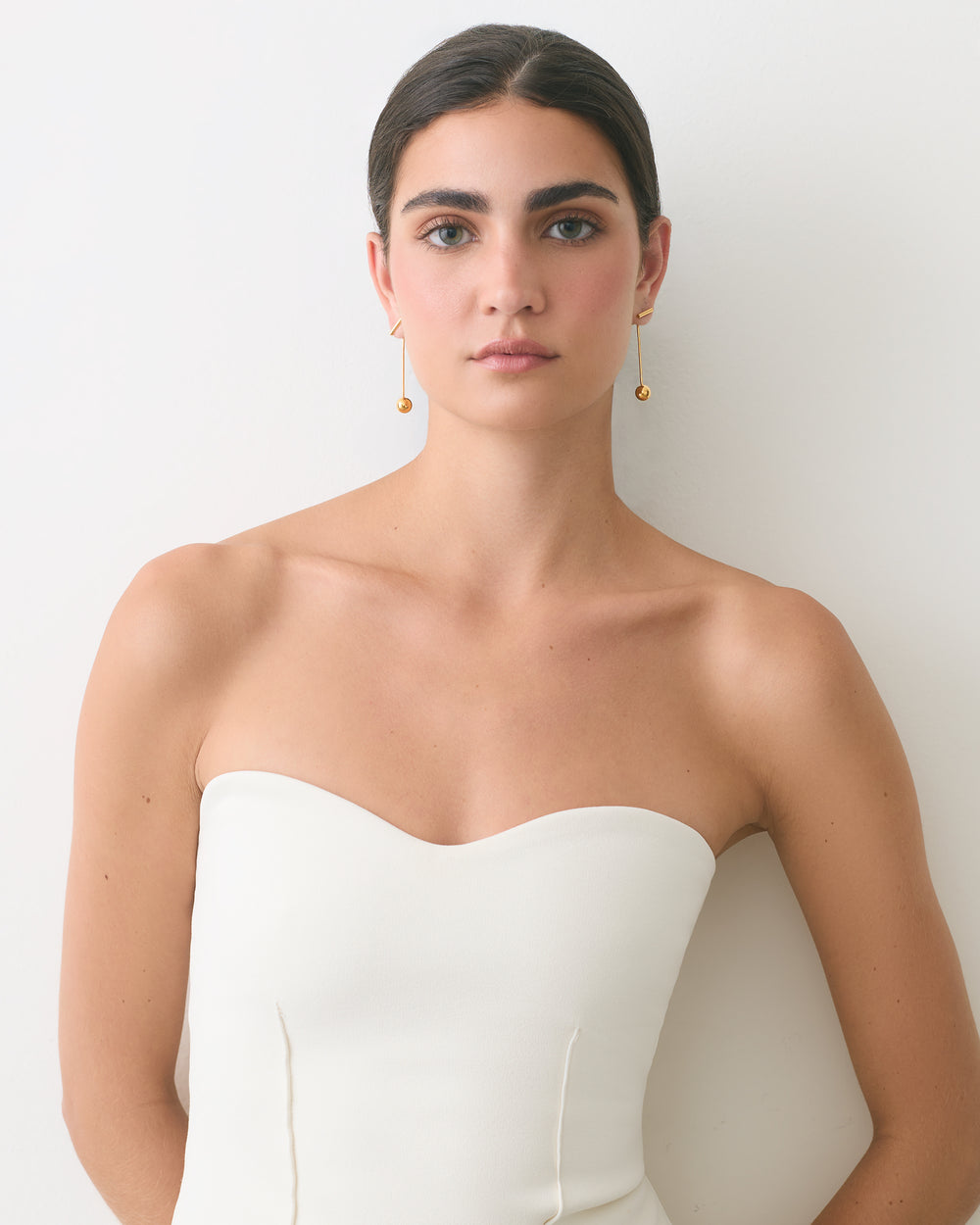 Person wearing a strapless top with drop earrings standing against a plain background.