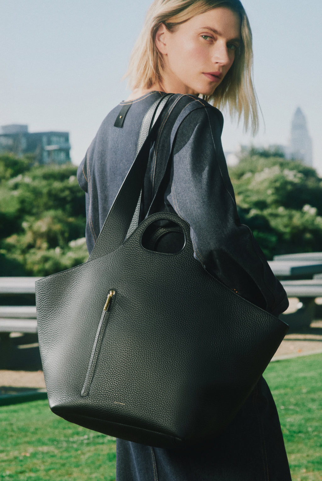Person carrying a large tote bag outdoors with greenery in background