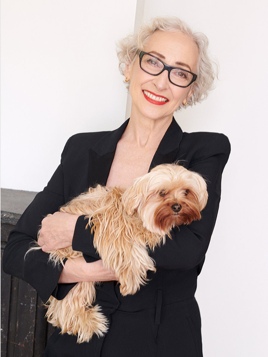 Person in glasses smiling and holding a small fluffy dog indoors.