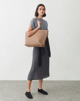 Person standing with a large shoulder bag wearing a long dress and shoes.