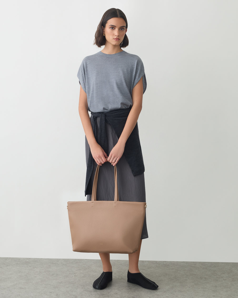 A person holding a tote bag with a sweater tied at the waist.
